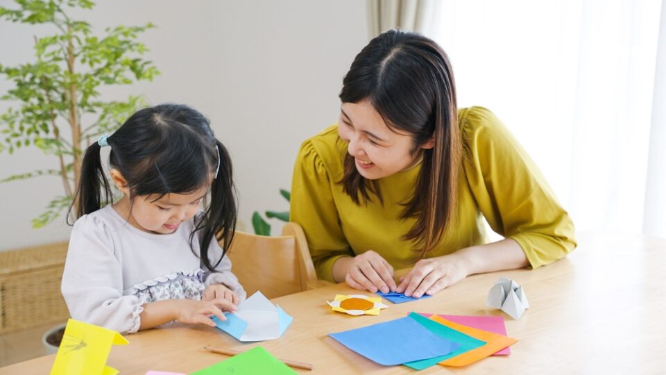A mother and daughter practicing origami with colored paper at a table.