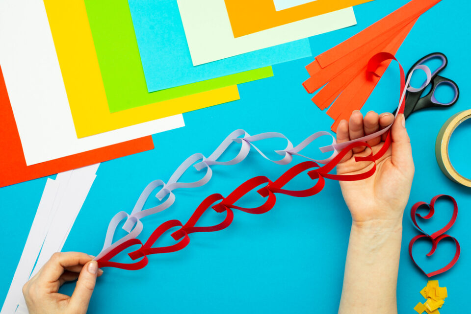 A pair of hands holding a heart-shaped garland made of red and white paper.