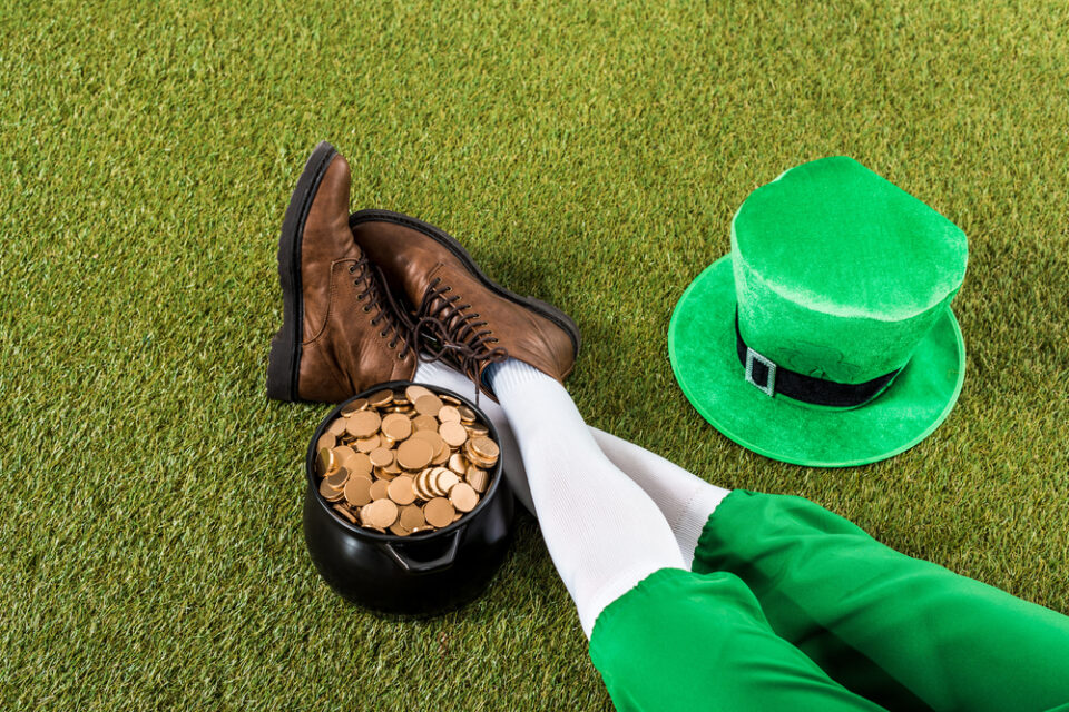 A sitting leprechaun’s feet and legs next to a pot of gold coins