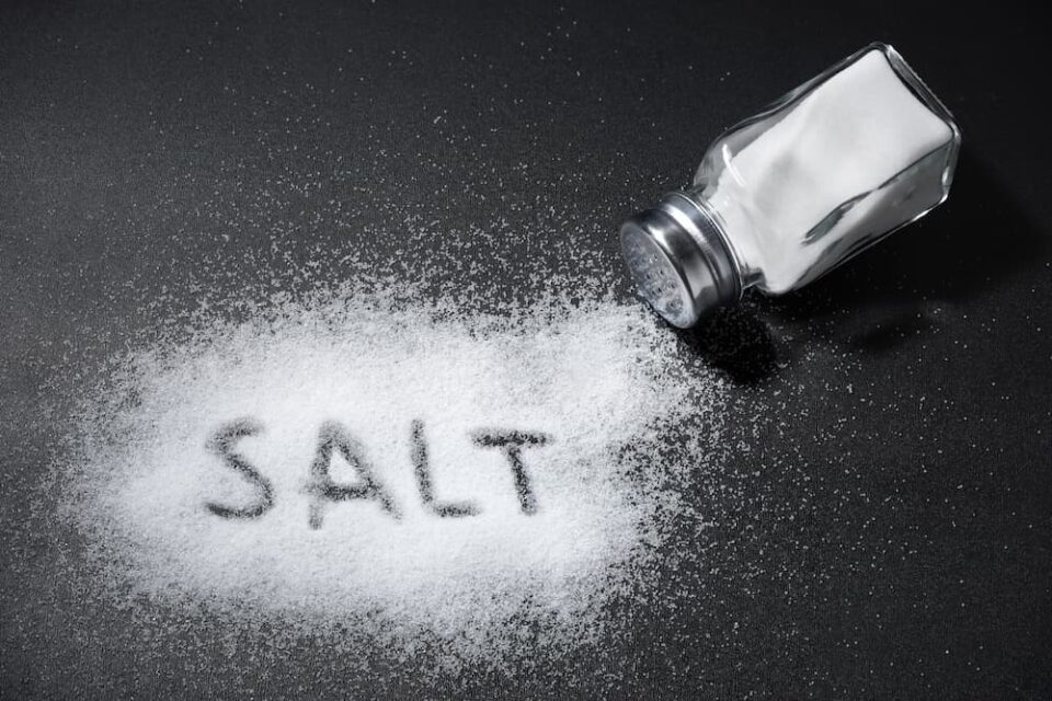 The word salt written in a pile of white salt, with a salt shaker tipped over next to it