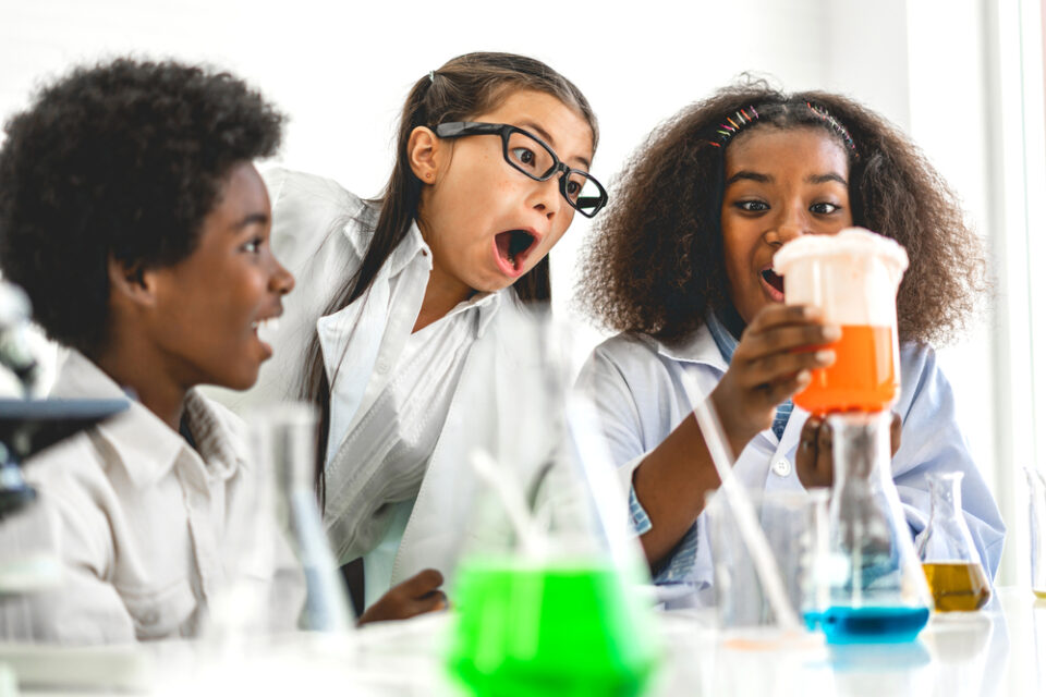 Three excited kids looking at a chemical reaction in a classroom.