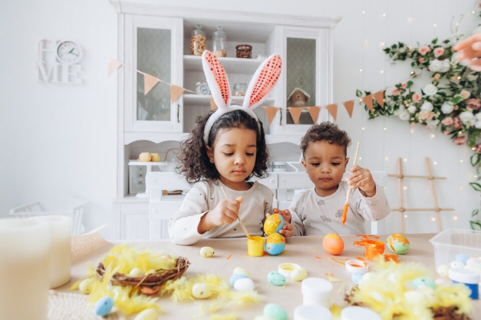 Two children decorate eggs with orange and yellow paint.