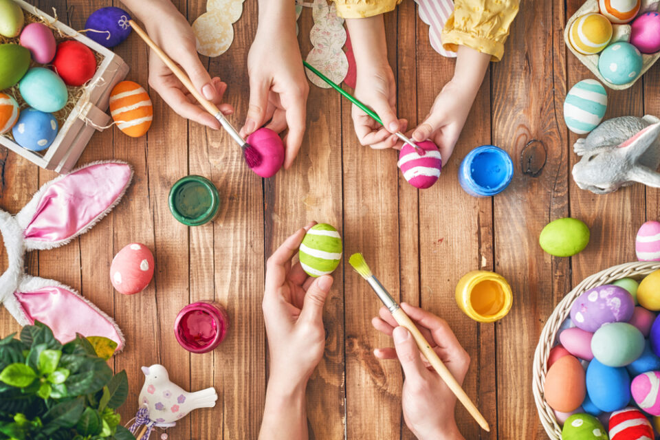 Hands painting colorful Easter eggs on a wooden table