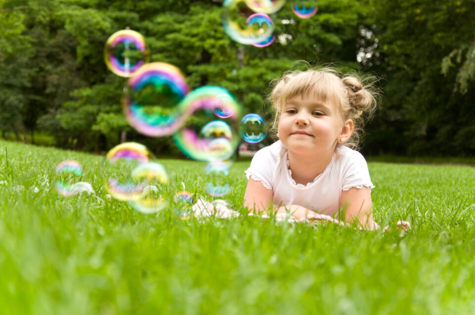 A young girl lying in the grass and looking at soap bubbles.