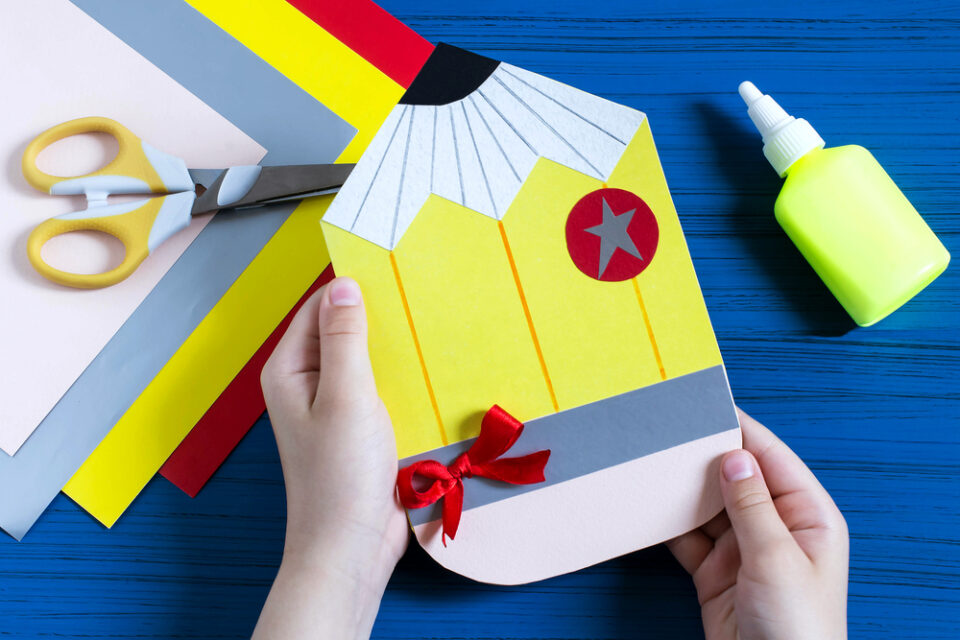 A child holding a DIY greeting card shaped like a pencil