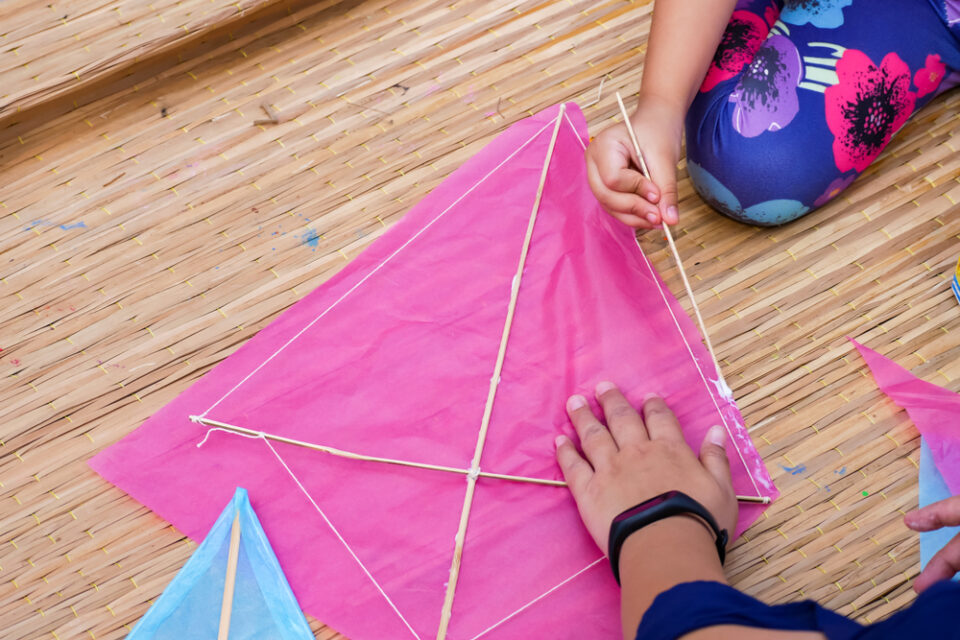 A child making a kite with pink tissue paper.