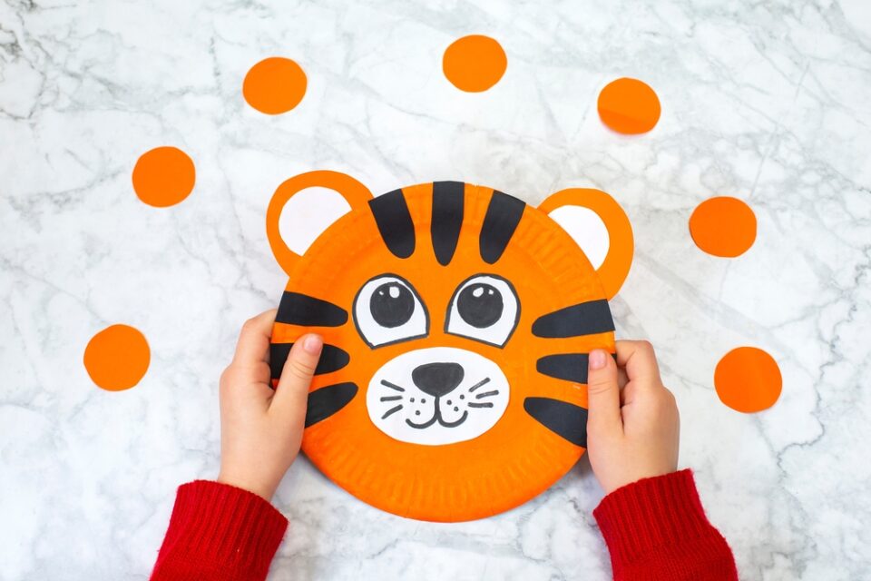 A child’s hands holding a paper plate tiger on a marble counter.