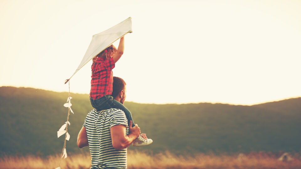 A father and child flying a kite during sunset.