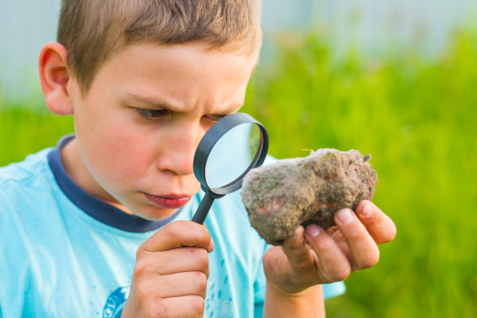 A young boy examining a rock with a magnifying glass