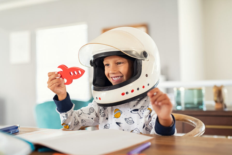 A young boy in an astronaut helmet playing with a toy rocket
