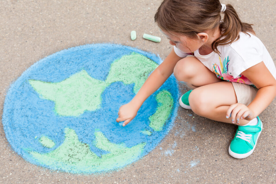 A young girl draws Earth with sidewalk chalk outside
