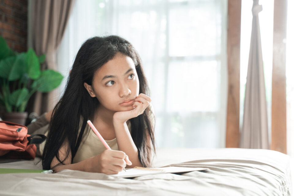 A young girl journals while lying on her bed