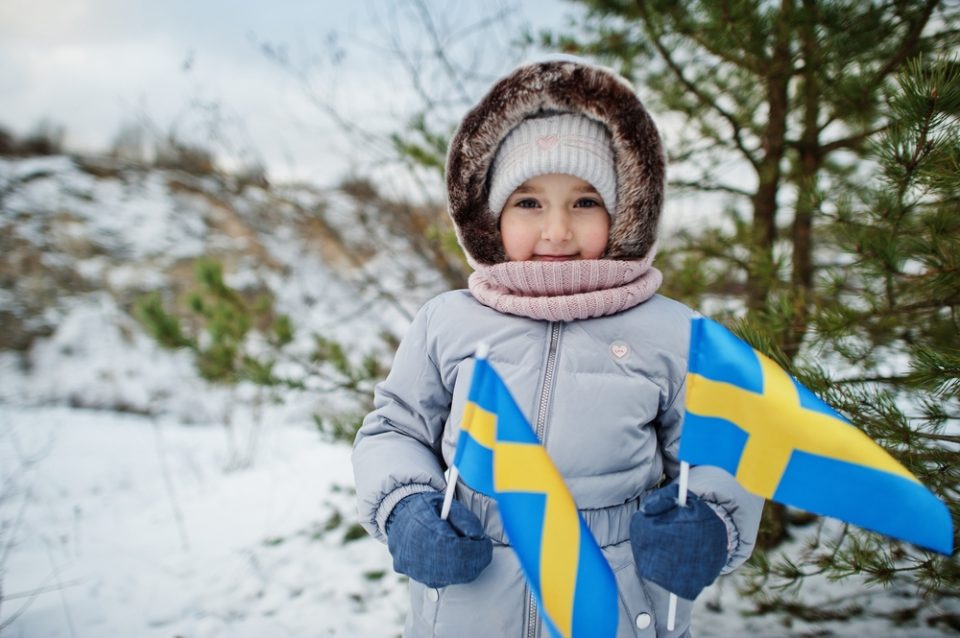 A child outdoors in the winter carrying two small Swedish flags
