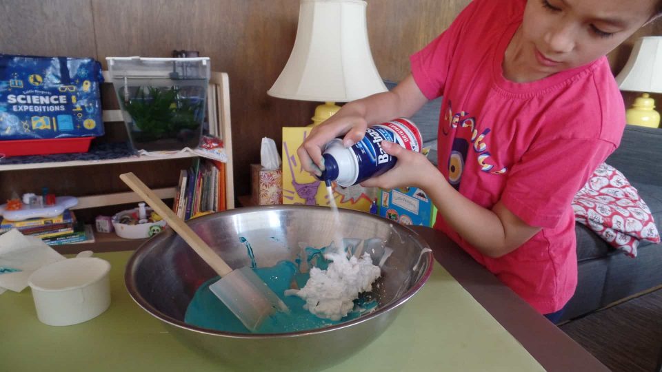 A child adding shaving cream to their fluffy slime mixture