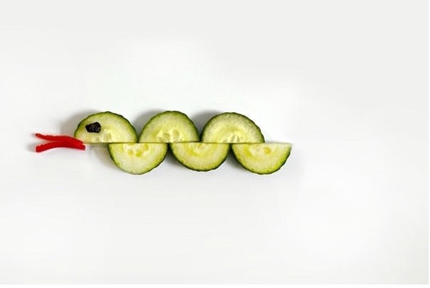 Six half cucumber slices arranged to look like an undulating snake with strips of red bell pepper as a tongue and a raisin for an eye.